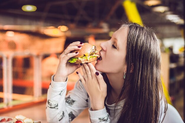 Foto mulher jovem comendo hambúrguer mulher comendo junk food, hambúrguer de comida gordurosa