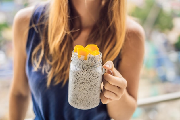 Foto mulher jovem comendo pudim de chia na varanda com vista para a cidade grande