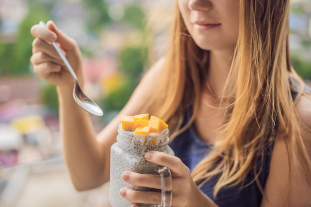 Mulher jovem comendo pudim de chia na varanda com vista para a cidade grande