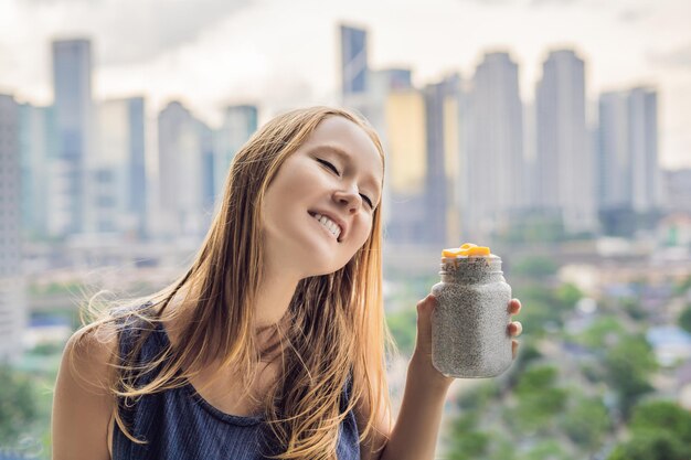 Mulher jovem comendo pudim de chia na varanda com vista para a cidade grande