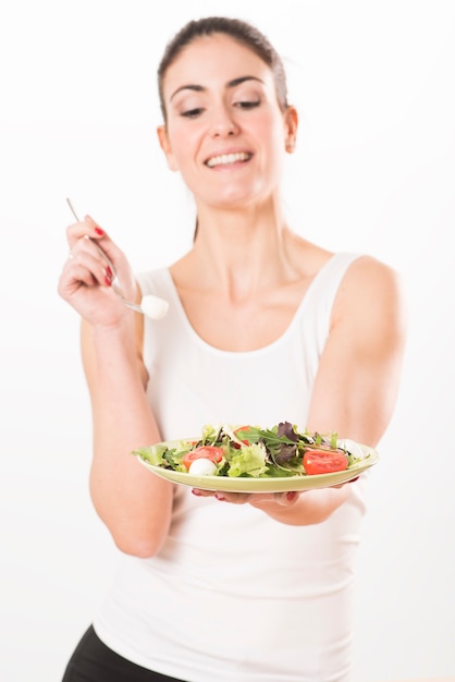 Mulher jovem comendo salada e segurando uma salada mista