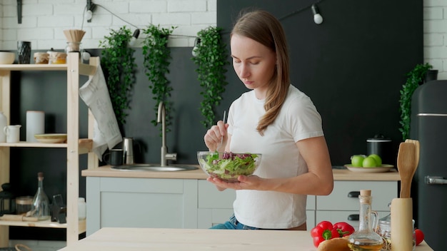 Mulher jovem comendo salada na cozinha de casa