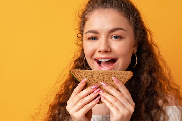 Foto mulher jovem comendo sanduíche contra um fundo amarelo