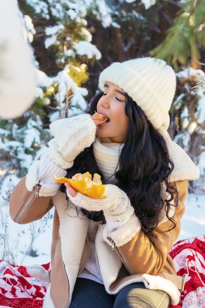 Mulher jovem comendo tangerina na floresta de inverno