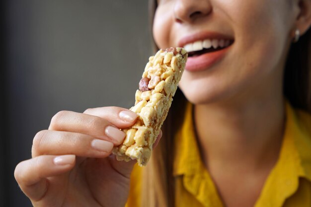 Mulher jovem comendo uma barra de cereais de nozes sem açúcar em fundo cinzento