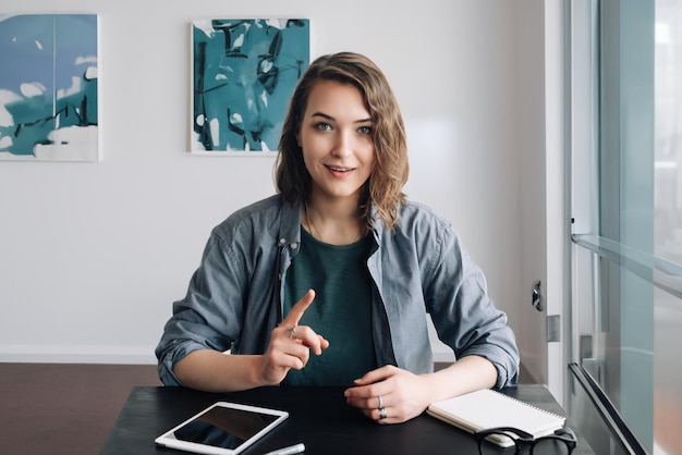 Mulher jovem confiante participando de uma videoconferência se comunicando através da câmera da Web do Office o