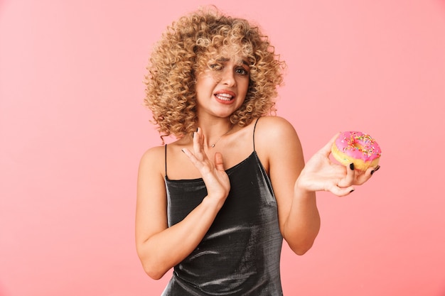 Foto mulher jovem confusa com cabelo encaracolado, recusa-se a comer donuts com cobertura