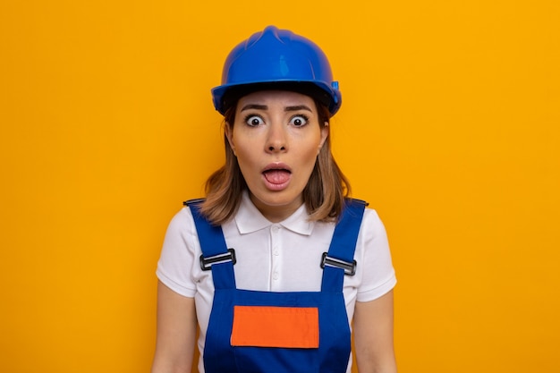 Mulher jovem construtora em uniforme de construção e capacete de segurança preocupada e confusa em pé na laranja