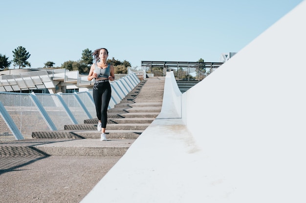 Mulher jovem correndo para perder peso após iniciar novos hábitos e atividades. Copie o espaço, mulher ouvindo música durante o treinamento em um lugar urbano da cidade. Leggins e tecido esportivo de alta qualidade, conceito de vida saudável