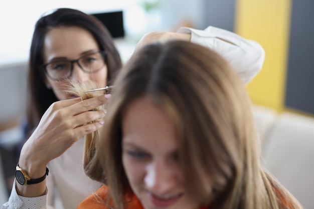 Mulher jovem cortando as pontas do cabelo com uma tesoura para a amiga em casa, closeup