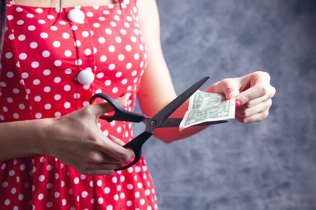 Mulher jovem cortando notas de um dólar com uma tesoura