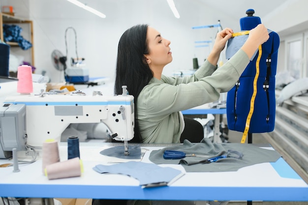 Mulher jovem costureira costura roupas na mesa de trabalho Costureira sorridente e sua mão fechada na oficina