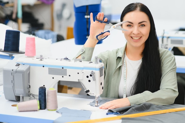 Mulher jovem costureira costura roupas na mesa de trabalho Costureira sorridente e sua mão fechada na oficina