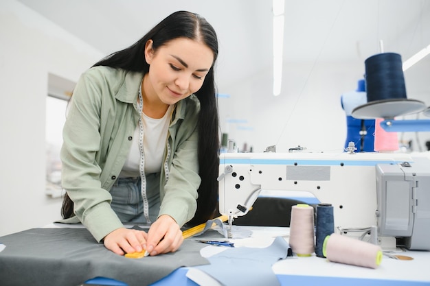 Mulher jovem costureira costura roupas na mesa de trabalho Costureira sorridente e sua mão fechada na oficina