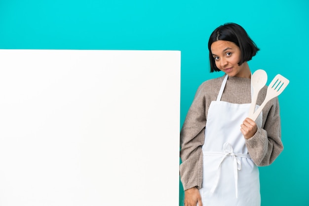 Mulher jovem cozinheira de raça mista com um grande cartaz isolado em um fundo azul rindo