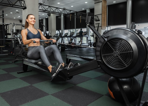 Mulher jovem cross fit funciona em uma máquina de remo no ginásio moderno. Treino funcional. Estilo de vida saudável