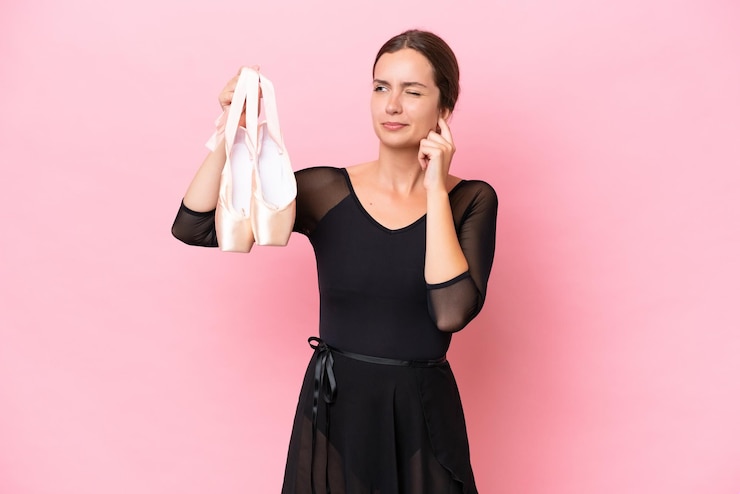 Foto mulher jovem dança caucasiana fazendo balé isolado no fundo rosa frustrado e cobrindo as orelhas