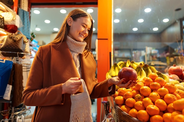 Mulher jovem de boa aparência em frente a prateleiras de frutas comprando mantimentos na rua