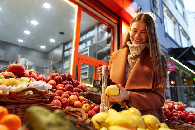 Foto mulher jovem de boa aparência em frente a prateleiras de frutas comprando mantimentos na rua