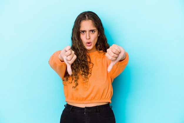 Mulher jovem de cabelo encaracolado caucasiano isolada mostrando o polegar para baixo e expressando antipatia.