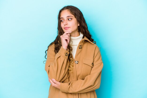 Mulher jovem de cabelo encaracolado caucasiano isolada olhando de soslaio com expressão duvidosa e cética.