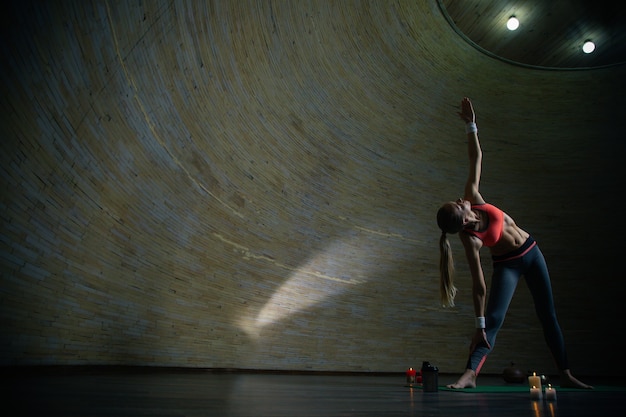 Mulher jovem de cabelos compridos praticando ioga em uma sala esférica e fazendo pose de triângulo com uma mão para cima