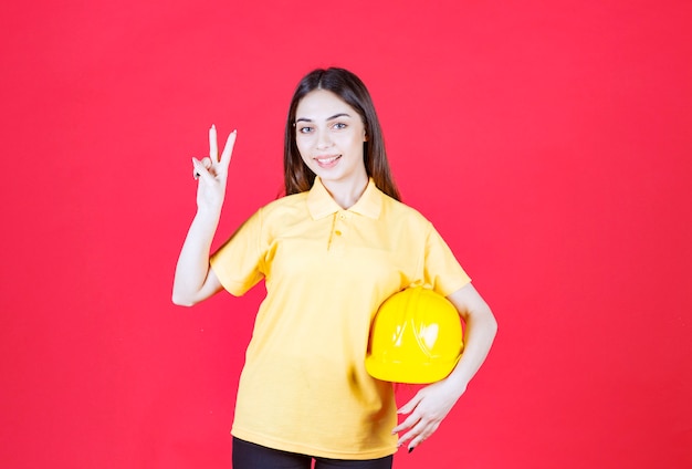 Mulher jovem de camisa amarela segurando um capacete amarelo e aproveitando o produto