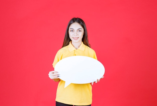 Mulher jovem de camisa amarela segurando um quadro oval de informações