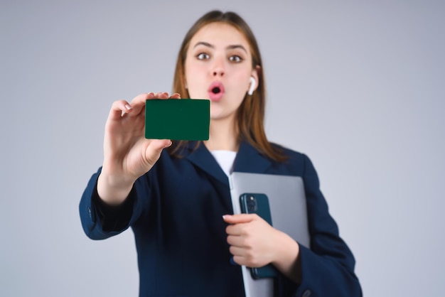 Foto mulher jovem de camisa branca segurando cartão de crédito perto do rosto e laptop isolado sobre fundo cinza