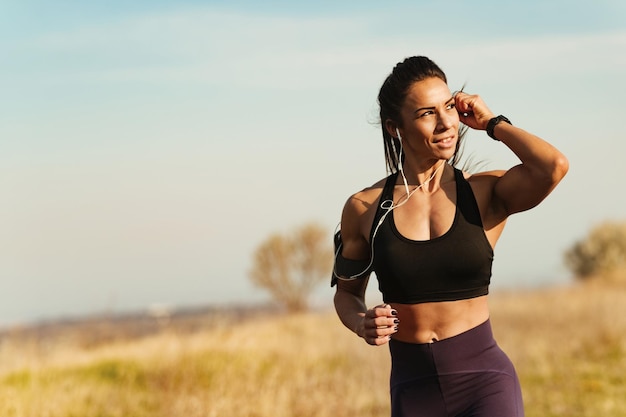 Mulher jovem de construção muscular ajustando fones de ouvido enquanto corre na natureza Copie o espaço