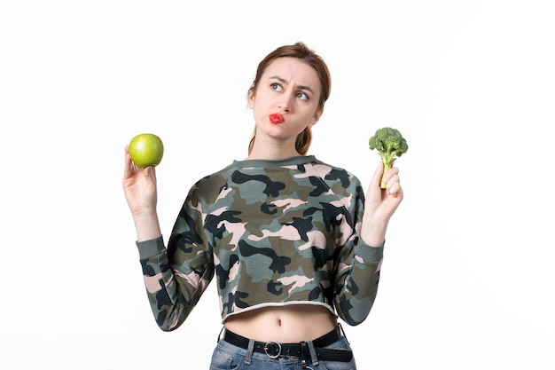 Mulher jovem de frente, segurando uma maçã verde e um pouco de brócolis no fundo branco, pele, bem-estar, saúde, horizontal, suco, fruta