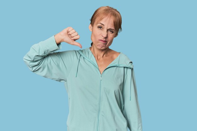 Mulher jovem de meia-idade em roupas esportivas no estúdio mostrando o polegar para baixo conceito de decepção