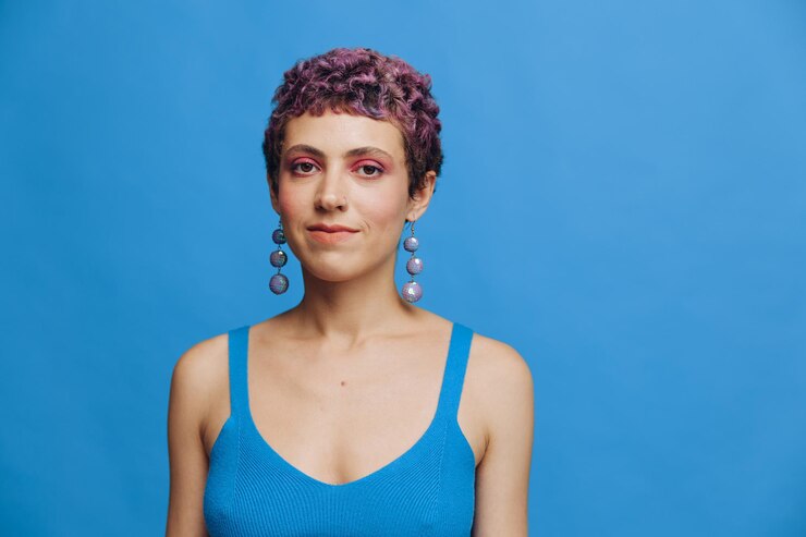 Foto mulher jovem de moda atlética com cabelos coloridos e corte de cabelo curto posando e dançando em roupas esportivas azuis sorrindo e olhando para a câmera closeup em um fundo monocromático azul