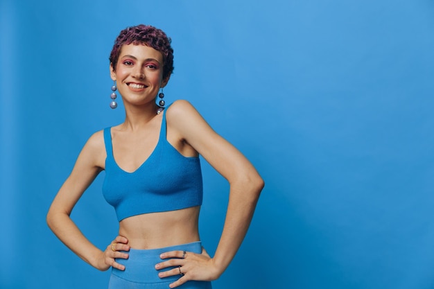 Mulher jovem de moda atlética posando em roupas esportivas azuis sorrindo e olhando para a câmera em um fundo monocromático azul