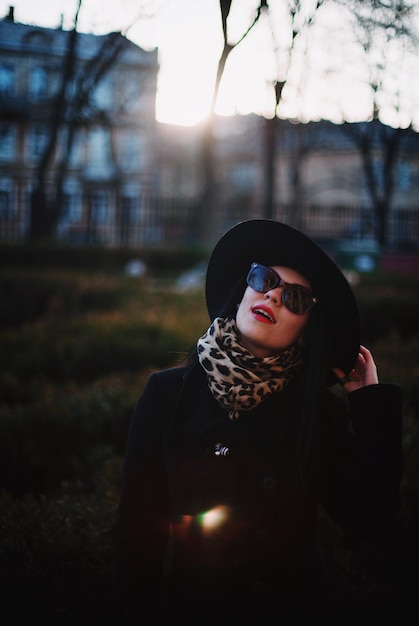Foto mulher jovem de moda vestindo chapéu e casaco de pé no parque