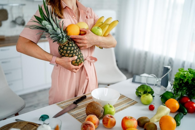 Mulher jovem de pé na cozinha com diferentes tipos de frutas Mulher nova de pé na culinária com diferentes tipo de frutas