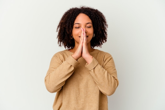 Mulher jovem de raça mista afro-americana isolada de mãos dadas orando perto da boca, sente-se confiante.