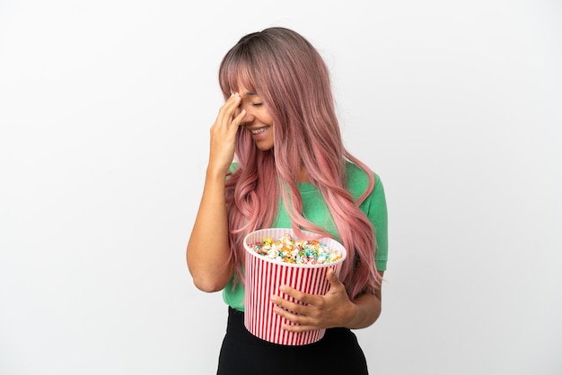 Mulher jovem de raça mista com cabelo rosa comendo pipoca isolada no fundo branco rindo