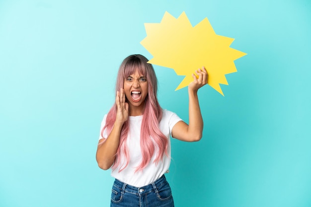 Foto mulher jovem de raça mista com cabelo rosa isolada em um fundo azul segurando um balão de fala vazio e gritando