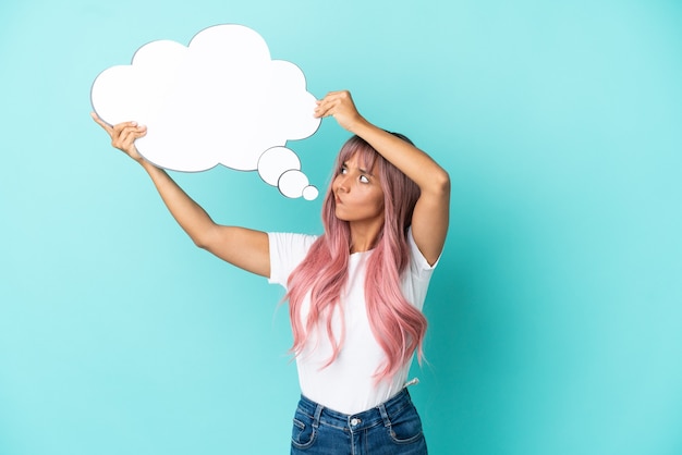 Foto mulher jovem de raça mista com cabelo rosa isolada em um fundo azul segurando um balão de fala