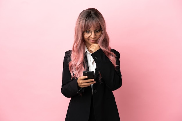 Mulher jovem de raça mista com cabelo rosa isolada em um fundo rosa pensando e enviando uma mensagem