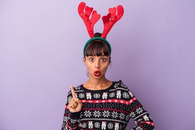 Mulher jovem de raça mista com chapéu de rena, comemorando o Natal, isolado no fundo roxo, tendo uma ótima ideia, o conceito de criatividade.