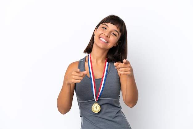 Mulher jovem de raça mista com medalhas isoladas em um fundo branco apontando o dedo para você enquanto sorri