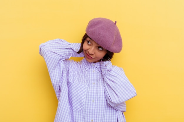 Mulher jovem de raça mista de boina isolada em fundo amarelo, esticando os braços, posição relaxada.