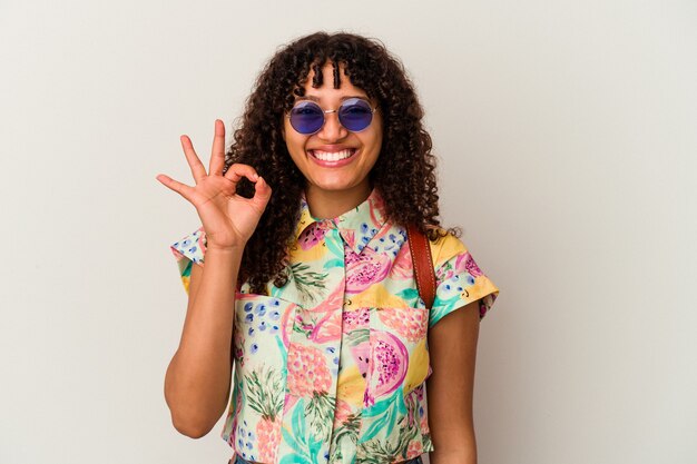 Mulher jovem de raça mista de óculos escuros, tirando férias isoladas, alegre e confiante, mostrando um gesto ok.