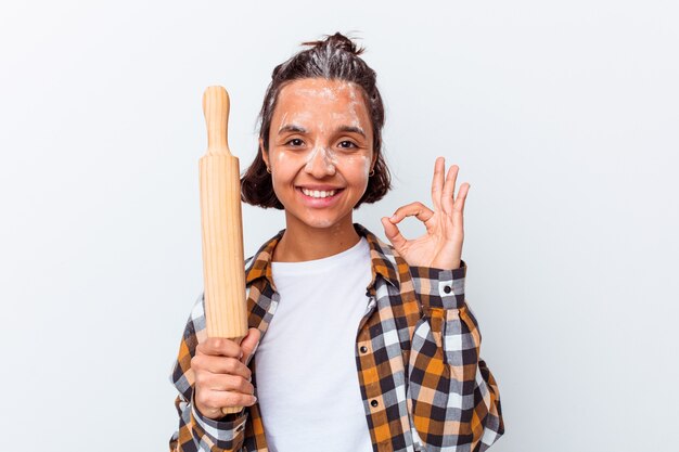 Mulher jovem de raça mista, fazendo pão isolado na parede branca, alegre e confiante, mostrando um gesto ok.