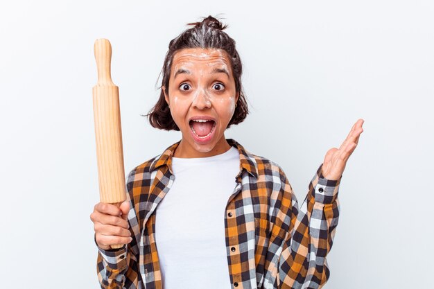 Mulher jovem de raça mista fazendo pão isolado na parede branca, recebendo uma agradável surpresa, animada e levantando as mãos.