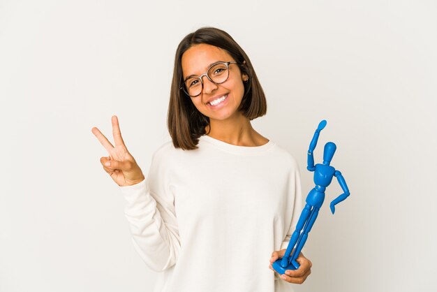 Mulher jovem de raça mista hispânica segurando uma boneca de madeira mostrando o número dois com os dedos.