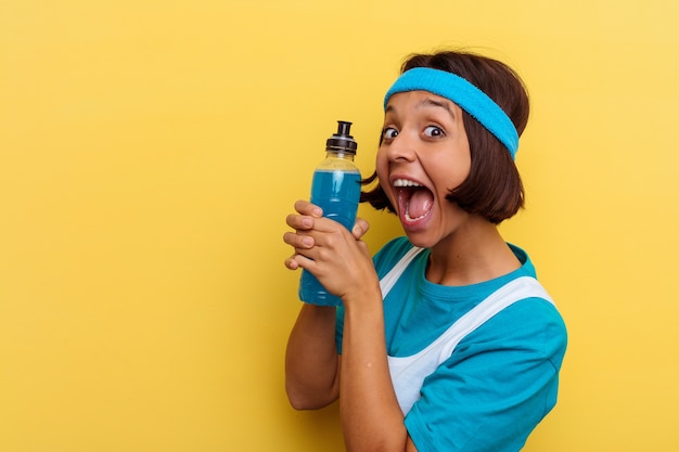 Mulher jovem de raça mista isolada bebendo uma bebida energética em fundo amarelo