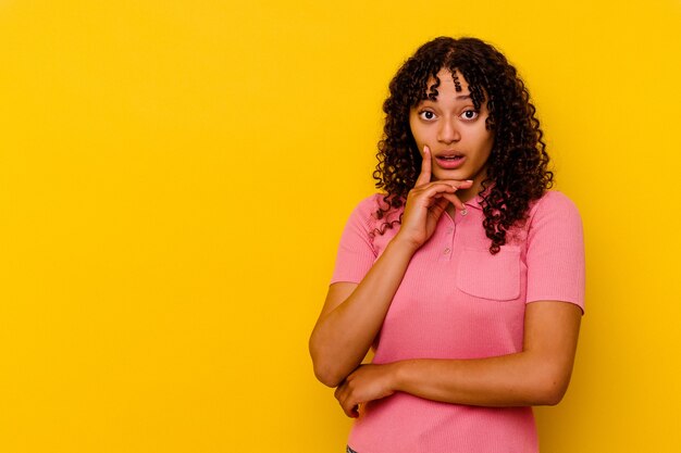 Mulher jovem de raça mista isolada em amarelo, olhando de soslaio com expressão duvidosa e cética.